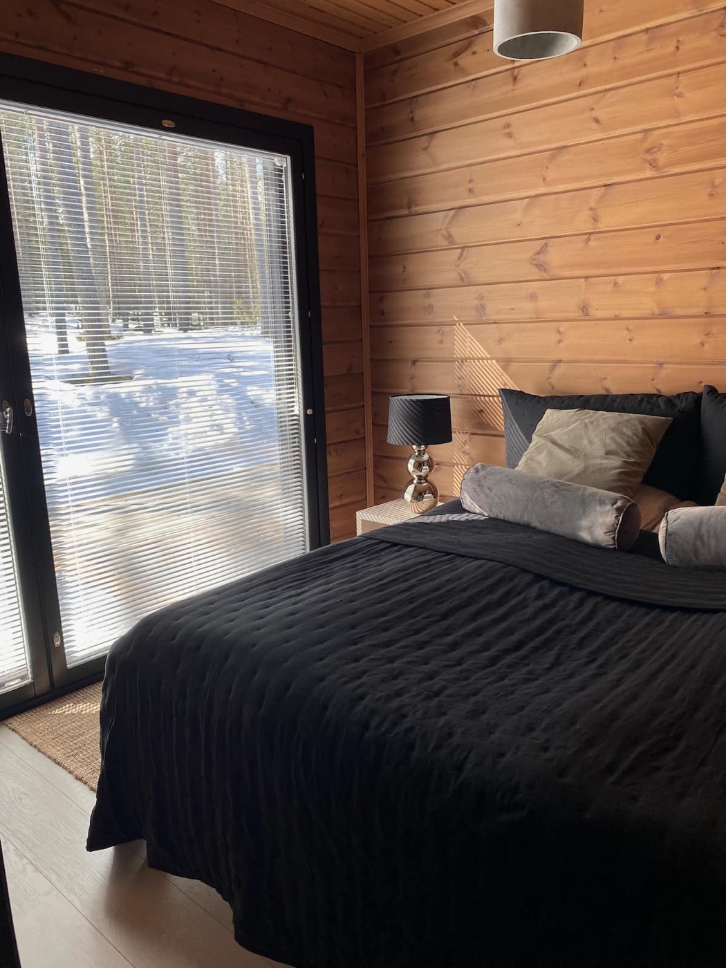 Bedroom 1 with a queen bed beside a tall window onto the forest