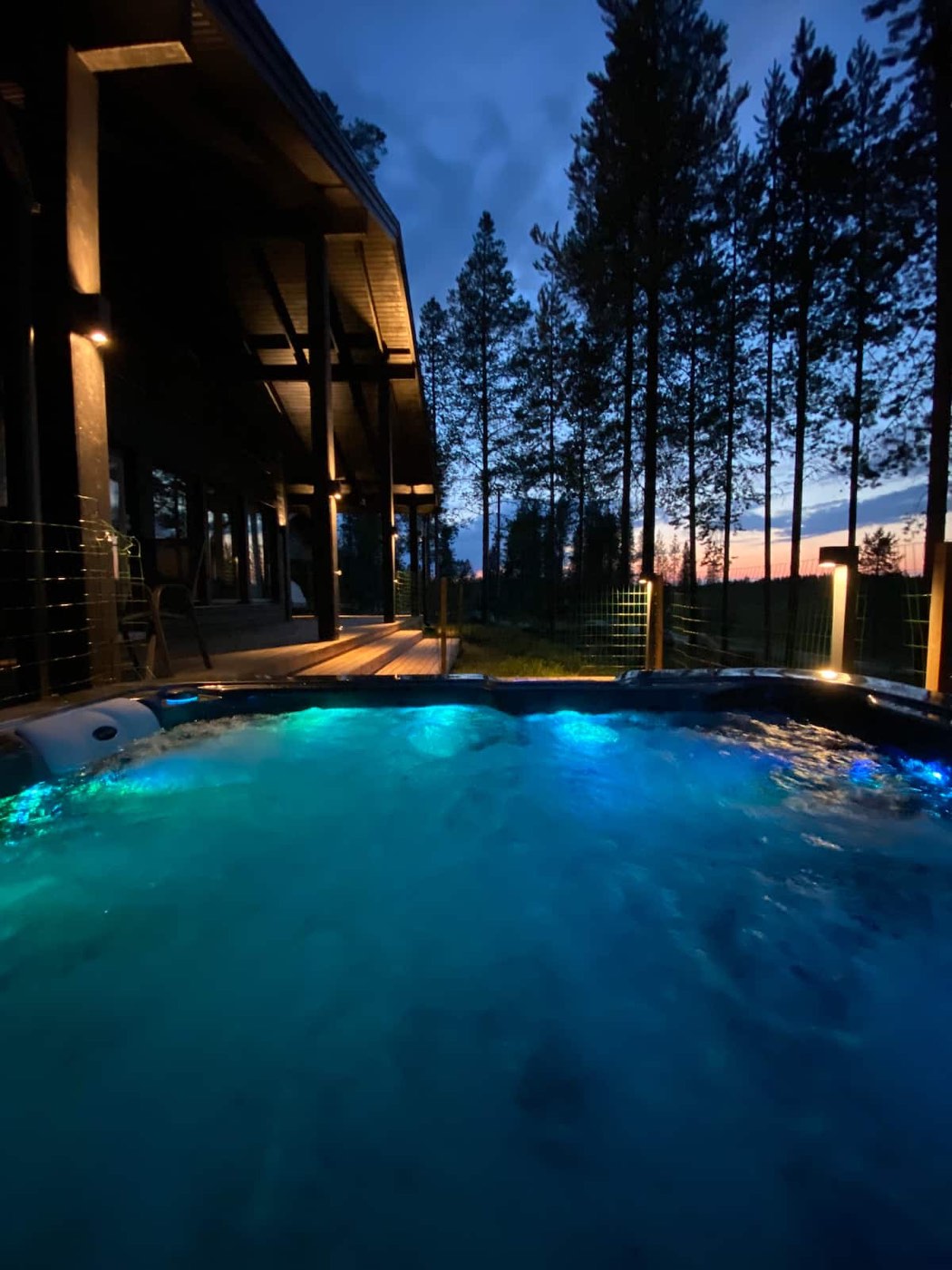 Hot tub lit turquoise at dusk under tall pines