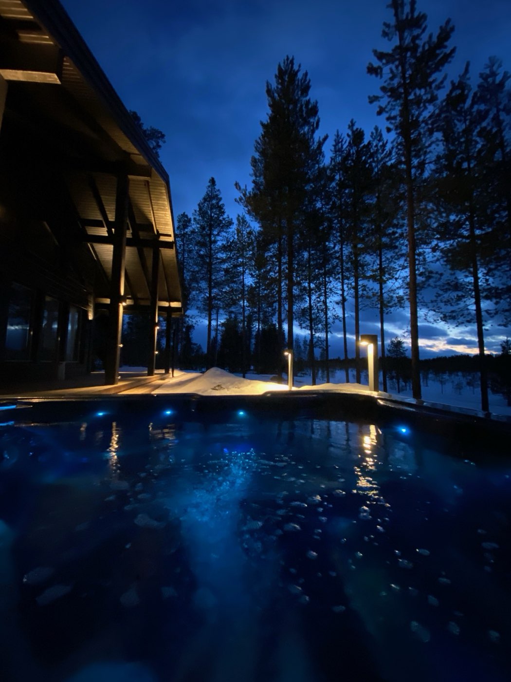 Outdoor hot tub glowing blue at dusk beside the house and pines