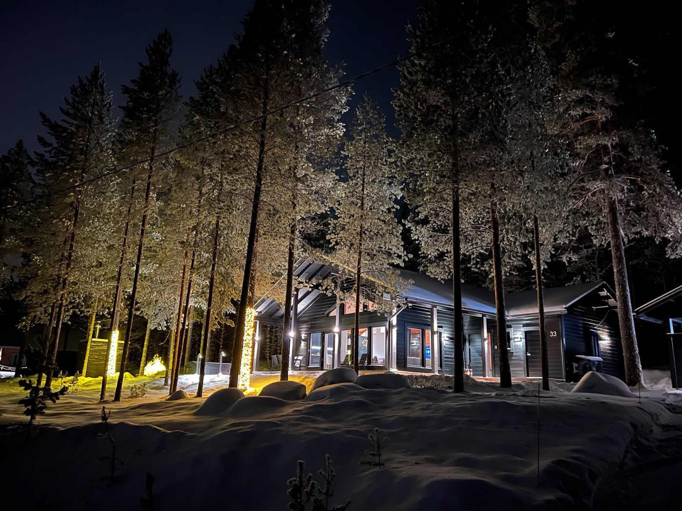 The Naava lit up at night among snow-covered pines, house number 33 by the door