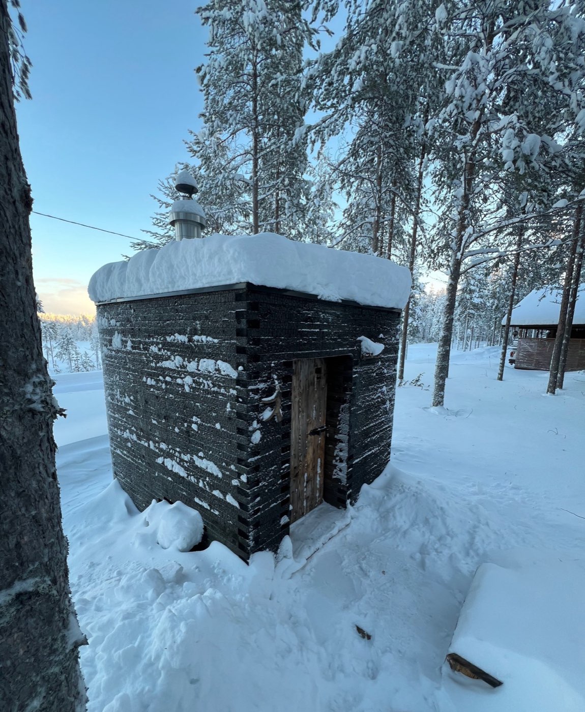 The black timber wood-burning sauna in the snowy yard